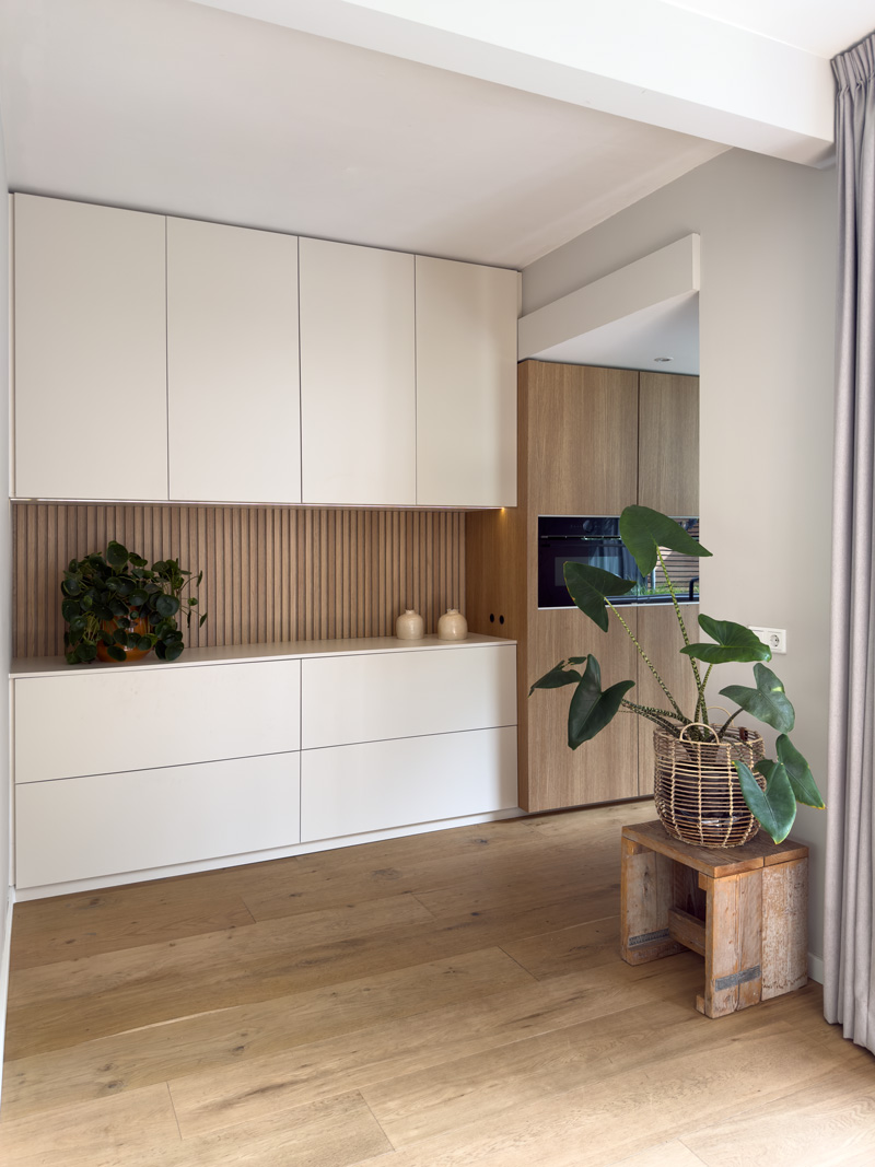 Keuken in Japandi stijl met beige deurtjes en houten latjes en een wankast met ovens.