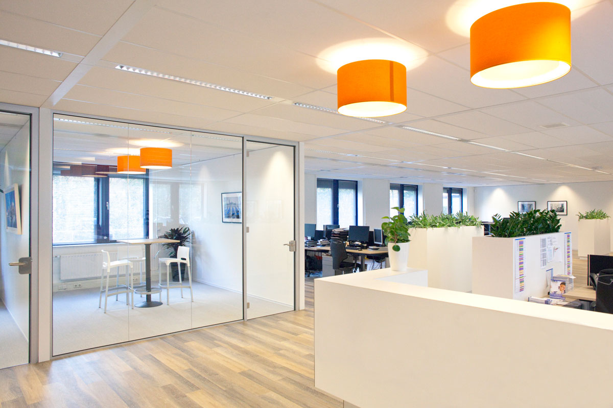 Inrichting kantoor in Zeist met glaswanden, houten vloeren en oranje hanglampen, voorzien van werkplekken en planten.
