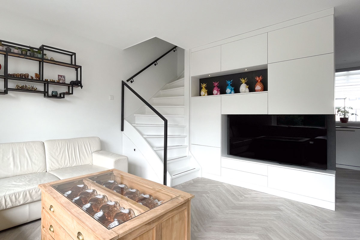Woonkamer met trap en kast op maat, een salontafel met wijnflessen.