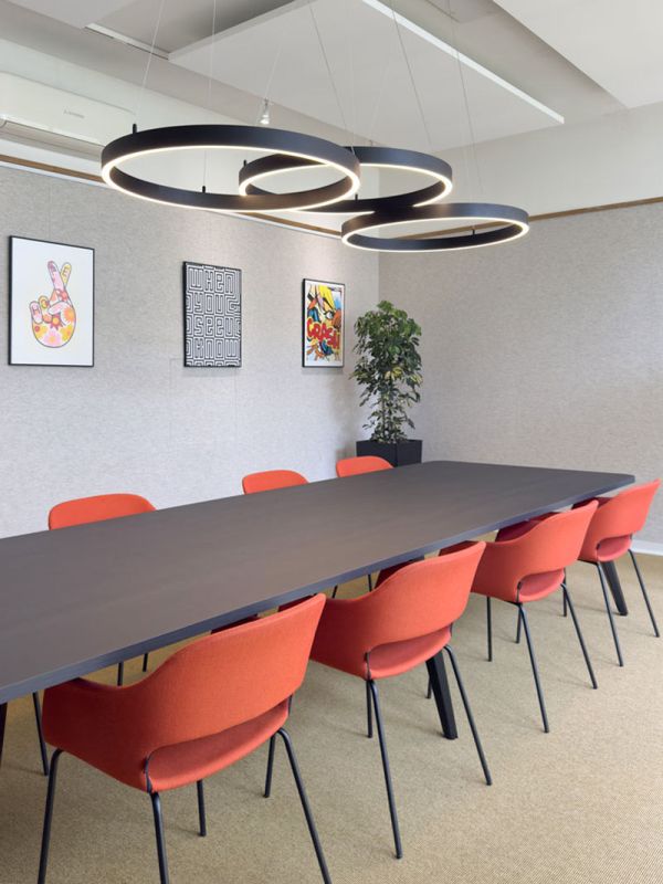 Vergaderzaal met oranje stoelen en zwarte ringlampen.