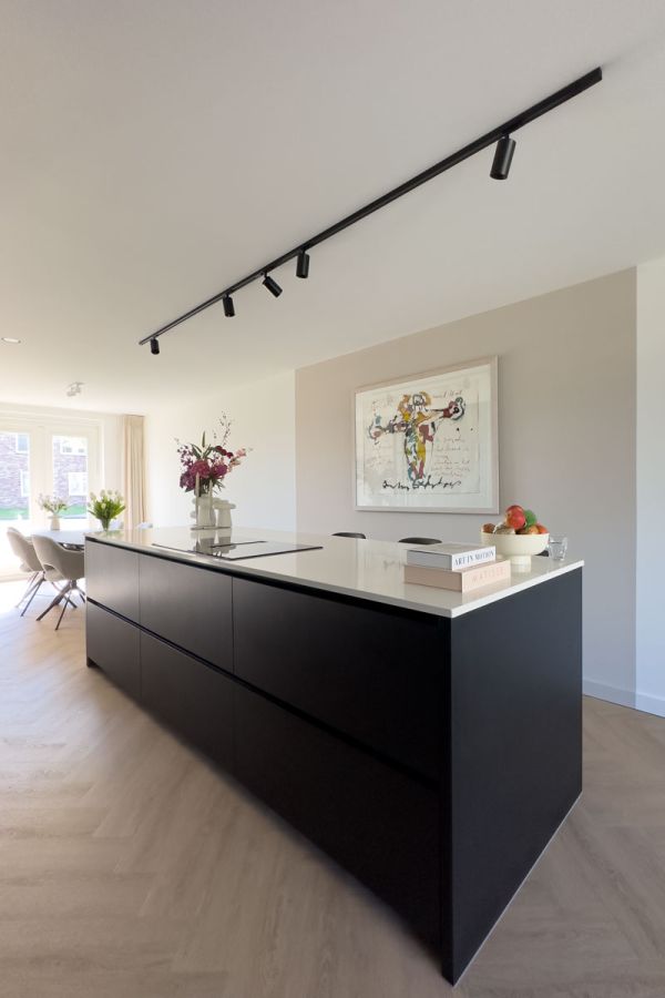 Detail van een grote luxe keuken met een marmeren werkblad, geïntegreerde champagnekoeler en een modern zwart wandmeubel met gouden accenten. Op de achtergrond een opvallend kunstwerk voor een unieke uitstraling.