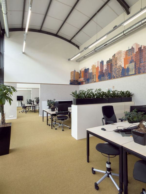 Open werkruimte en kantoortuin in industrieel kantoor met werkplekken, planten en signing op de hoge wanden.