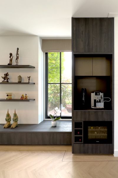Moderne zithoek met donker houten kast, zwevende planken en uitzicht op de tuin in een woning.