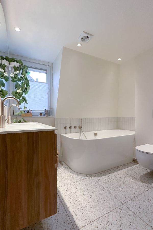 Moderne badkamer in jaren 30 woning met dubbele wastafel, ronde spiegel en terrazzo vloer.